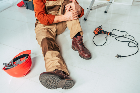 cropped view of repairman sitting on floor and holding injured knee in officeの写真素材