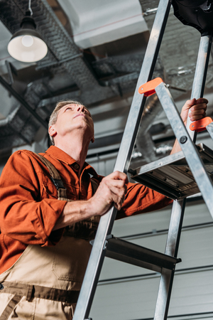 repairman in orange uniform standing on ladder in garageの写真素材