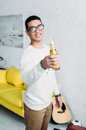 smiling handsome mixed race man holding bottle of beer and looking at cameraの写真素材