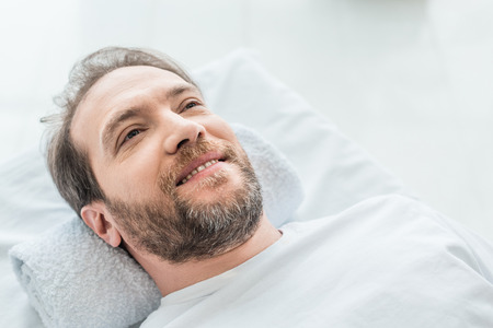 smiling bearded male patient lying on massage table in medical officeの写真素材