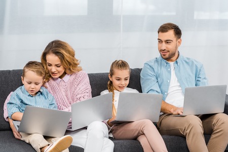 happy family sitting on sofa and using laptops in apartmentの写真素材