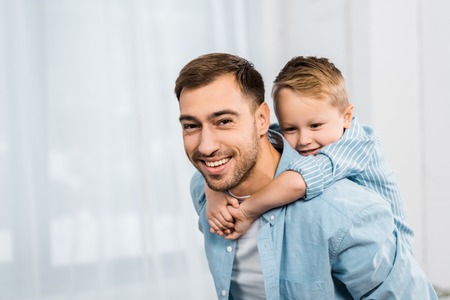 smiling father holding cute son on shoulders and looking at camera