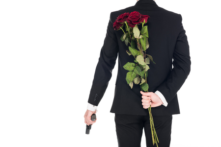 back view of killer in black suit holding handgun and red rose flowers, isolated on whiteの写真素材