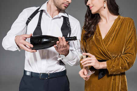 cropped view of boyfriend pouring champagne for girlfriend isolated on greyの写真素材