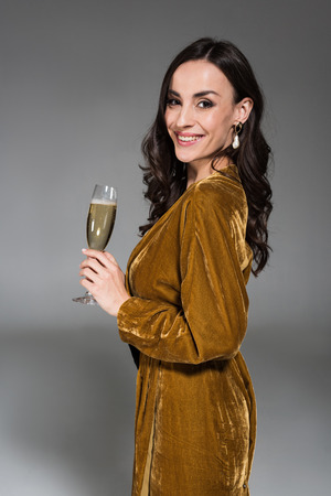 beautiful smiling woman in golden dress holding glass of champagne isolated on greyの写真素材