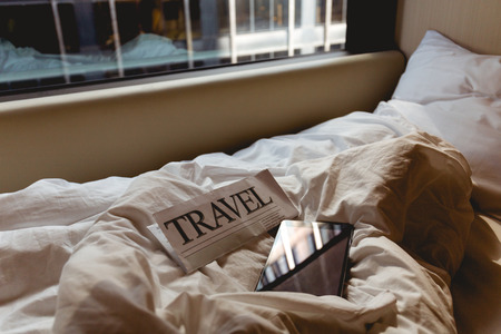 close up view of travel newspaper and tablet on bed in hotel roomの写真素材