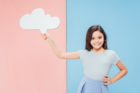 adorable child holding speech bubble and looking at camera on blue and pink backgroundの写真素材