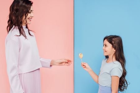 adorable child giving candy to woman on blue and pink backgroundの写真素材