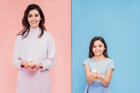 beautiful woman and child holding cupcakes and looking at camera on blue and pink background