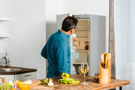 rear view of mature man looking into open fridge in kitchenの写真素材