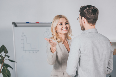 cheerful mature businesswoman looking at bearded young businessman in eyeglassesの写真素材