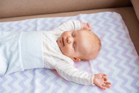 adorable newborn baby with closed eyes and raised hands lying on sofa
