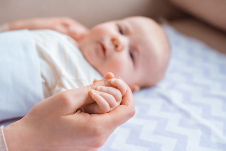 cropped shot of mother holding hand on adorable infant kid lying on couchの写真素材