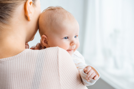 back view of young mother carrying adorable baby at homeの写真素材