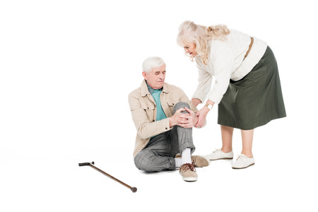 retired man holding knee while having arthritis pain near caring wife isolated on whiteの写真素材