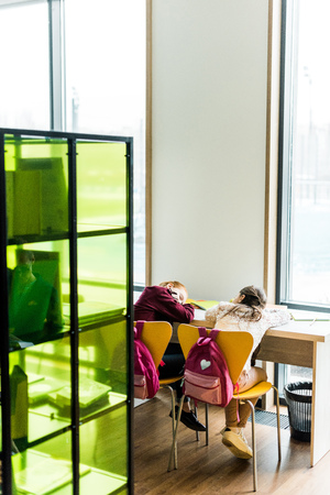 back view of bored schoolgirls sleeping on desk in library