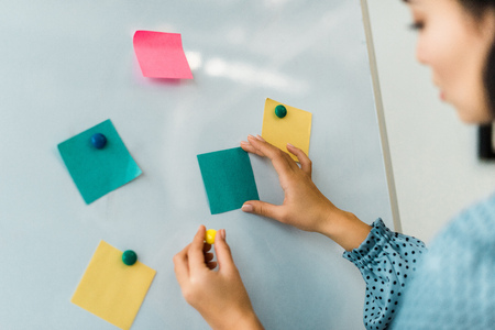 cropped view of woman putting colorful sticky notes on white board in officeの写真素材