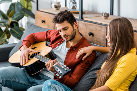 young girl sitting on sofa with boyfriend while listening to guitar musicの写真素材