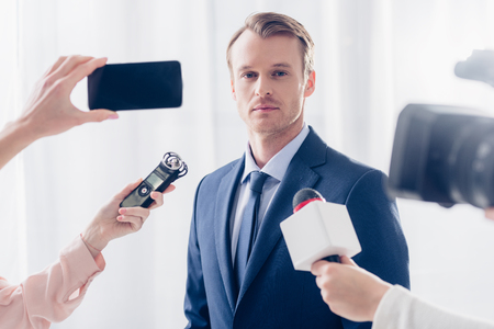 handsome businessman giving interview to journalists and looking at camera in officeの写真素材