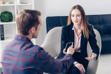 young beautiful businesswoman in suit giving interview to journalist in officeの写真素材