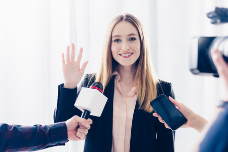 smiling attractive businesswoman giving interview to journalists and waving hand in office