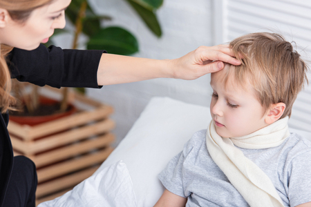 mother taking care of sick son and touching his forehead in bedroomの写真素材