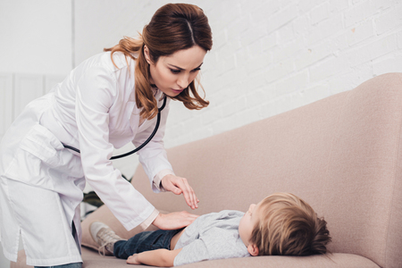 pediatrist palpating sick boy stomach on sofa in living roomの写真素材