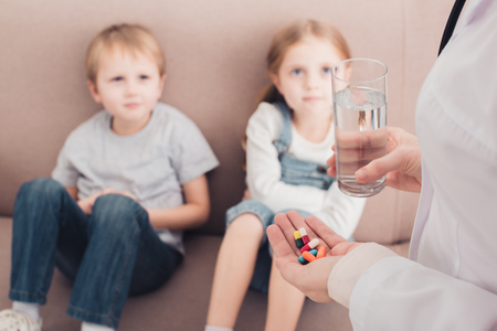 cropped image of pediatrist holding pills and glass of water for sick children in living roomの写真素材