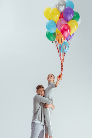 beautiful couple hugging while woman holding bundle of colorful balloons isolated on greyの写真素材