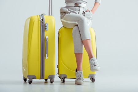 cropped view of woman sitting on suitcases with crossed legs on grey background, travel conceptの写真素材