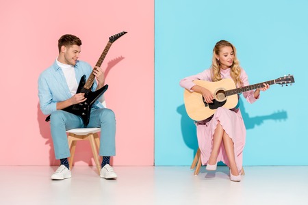 beautiful couple playing electric and acoustic guitars on pink and blue background