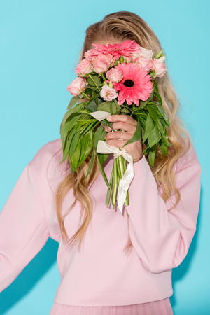 woman in pink clothing hiding behind beautiful bouquet on blue backgroundの写真素材