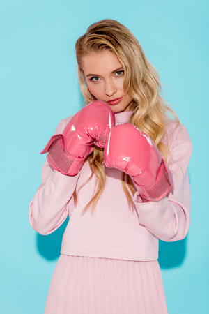 beautiful blonde woman looking at camera and posing in boxing gloves on turquoise backgroundの写真素材