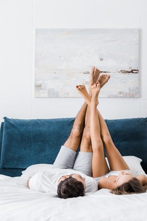 young boyfriend and girlfriend lying in white bed with raised legsの写真素材