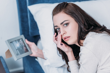 beautiful upset woman holding picture frame, crying and looking at camera at home