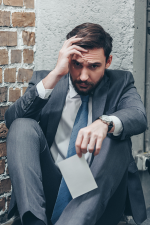upset man in grey suit sitting on floor and holding photo on brown textured background in room, grieving disorder conceptの写真素材