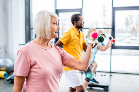 side view of senior sportswoman and her friends exercising with dumbbells at gymの写真素材