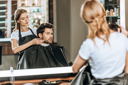 reflection in mirror of hairdresser doing hairstyle to handsome client in beauty salonの写真素材