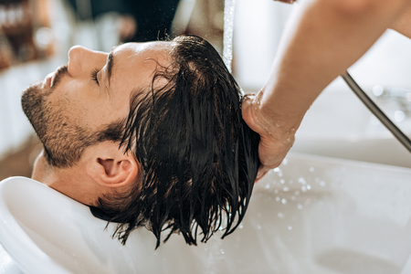 cropped shot of hairstylist washing hair to handsome young man in beauty salonの写真素材