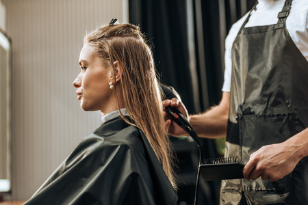 cropped shot of hairdresser holding hairbrush and drying hair to attractive girl in beauty salonの写真素材