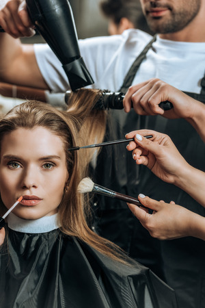 beautiful girl looking at camera while stylists applying makeup and doing hairstyleの写真素材