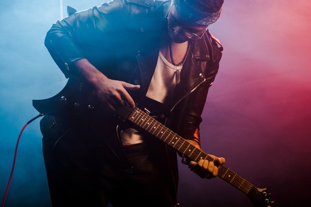 young male rocker in leather jacket performing on electric guitar on stage with smoke and dramatic lightingの写真素材