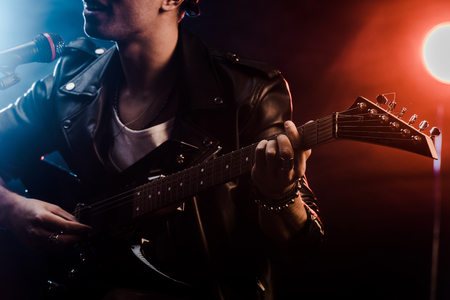 partial view of young man singing in microphone and playing on electric guitar on stage during rock concertの写真素材