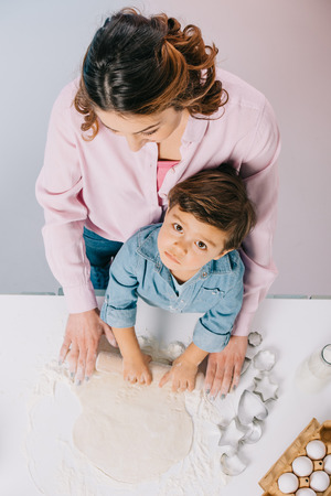 top view of mother with little son rolling out dough at kitchen table together on light backgroundの写真素材