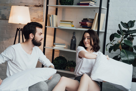 beautiful young couple in pajamas having pillow fight at homeの写真素材