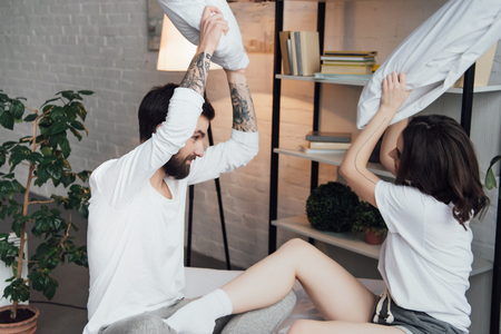 beautiful young couple in pajamas having fun and fighting with pillows at homeの写真素材