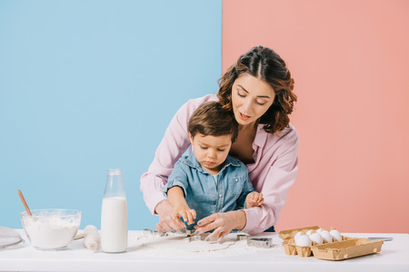 pretty mother and little son cutting figures in dough together on bicolor backgroundの写真素材