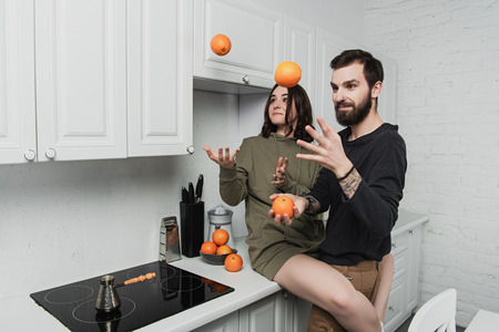 beautiful young couple having fun and juggling with oranges in kitchenの写真素材