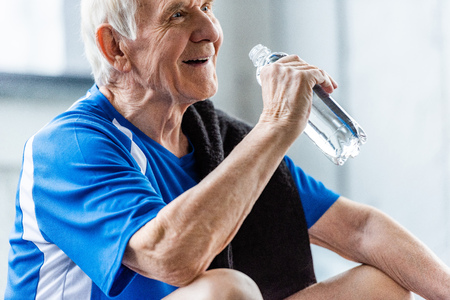 selective focus of happy senior sportsman with towel and bottle of water resting at gymの写真素材