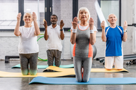 senior multicultural sportspeople synchronous exercising on fitness mats at gymの写真素材